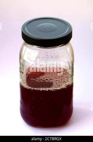 Versiegeltes Klarglas-Messglas mit vier Messmethoden und einem schwarzen Metalldeckel mit dunkelrotem Waldfruchtsaft halb voll oder halb leer Oz Stockfoto