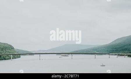 Eine lange Brücke auf dem Gewässer umgeben von Hügel mit Bäumen unter einem klaren Himmel bedeckt Stockfoto