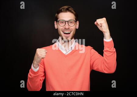 Portrait von positiv aufgeregt jungen bärtigen Mann in einer Brille macht ja Geste vor schwarzem Hintergrund Stockfoto
