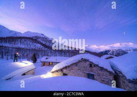 Fotograf fotografiert die verschneiten Hütten von Groppera in der Abenddämmerung, Madesimo, Valchiavenna, Valtellina, Lombardei, Italien Stockfoto