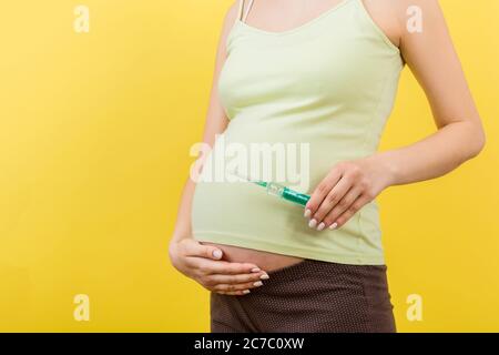 Nahaufnahme der Spritze für die Injektion in die Hand der schwangeren Frau auf farbenfrohem Hintergrund mit Kopierraum. Medizinische Behandlung während der Schwangerschaft Konzept. Stockfoto
