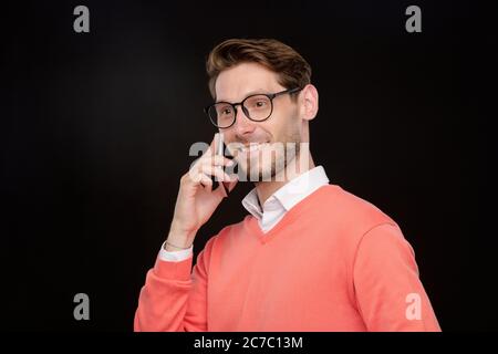 Lächelnd selbstbewusst junger Mann in hellen Pullover mit Telefongespräch vor schwarzem Hintergrund Stockfoto