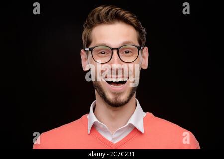 Porträt eines ekstatischen jungen Mannes mit Stoppeln, die eine Brille tragen und vor schwarzem Hintergrund stehen Stockfoto