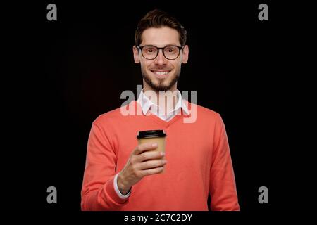 Portrait von positiven jungen Mann in orange Pullover trinken Kaffee vor schwarzem Hintergrund gehen Stockfoto