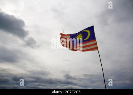 Fokussierte Aufnahme der malaysischen Nationalflagge mit grauen Wolken Im Hintergrund Stockfoto