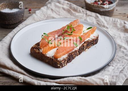 Roggenbrot mit geräuchertem Lachs, Frischkäse auf altem Holztisch. Smorrebrod Stockfoto