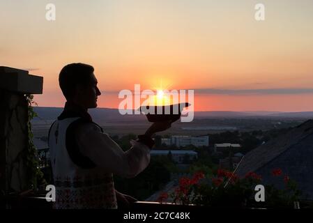 Profilaufnahme eines Mannes in traditioneller moldawischer Kleidung Sein Hut in seiner Handfläche während des Sonnenuntergangs Stockfoto