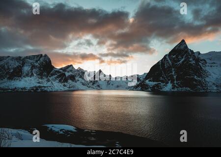 Die horizontale Aufnahme eines von Bergen umgebenen Wasserkörpers Bedeckt mit Schnee während des Sonnenuntergangs Stockfoto