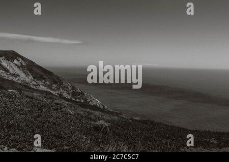 Graustufen Aufnahme von Hügeln mit Gras am Meer bedeckt Stockfoto