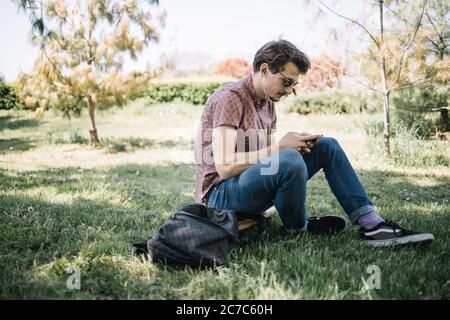 Porträt des Mannes mit einem Smartphone, während er auf dem Boden sitzt Stockfoto