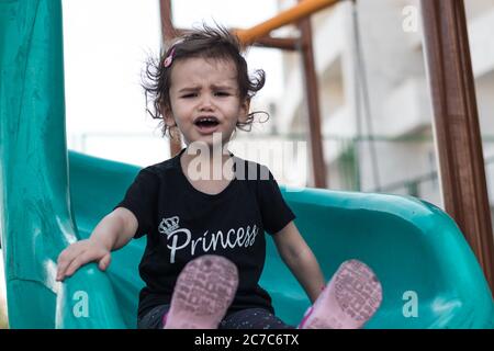 Ein launisch kleines Mädchen auf einer Rutsche auf einem Spielplatz. Stockfoto