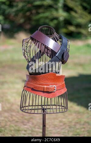 Vertikale selektive Aufnahme von orangefarbenen, schwarzen und braunen Gürteln auf einer kopflosen Schaufensterpuppe aus Metall Stockfoto