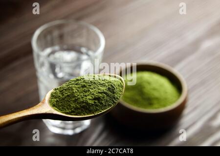 Weizengras oder Gerstengras Pulver in Holzlöffel und Glas Wasser. Detox Saft Vorbereitung. Stockfoto