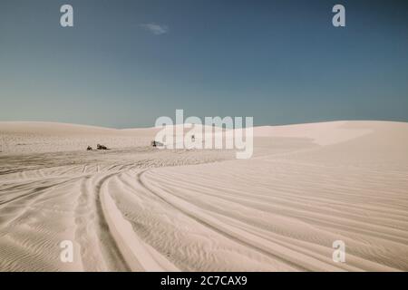 Landschaftsaufnahme einer Wüste mit Reifenspuren auf der Sand und Kraftfahrzeuge in der Ferne Stockfoto