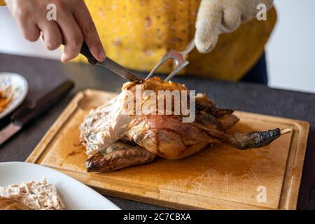Kaukasische Frau, die ein gebratenes Huhn auf einer Holzplatte mit einem Messer und einer Gabel schnitzt. Stockfoto