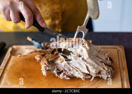 Kaukasische Frau, die ein gebratenes Huhn auf einer Holzplatte mit einem Messer und einer Gabel schnitzt. Stockfoto