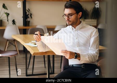 Junger seriöser Geschäftsmann in Brillen nachdenklich mit Papieren im Büro arbeiten Stockfoto