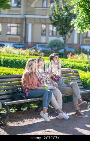 Drei junge Freunde sitzen auf der Bank im Hof trinken Kaffee Stockfoto