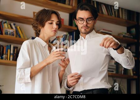 Junge, nachdenkliche Kollegen aus der Wirtschaft stehen mit Papieren und diskutieren gemeinsam im Büro über neue Projekte Stockfoto