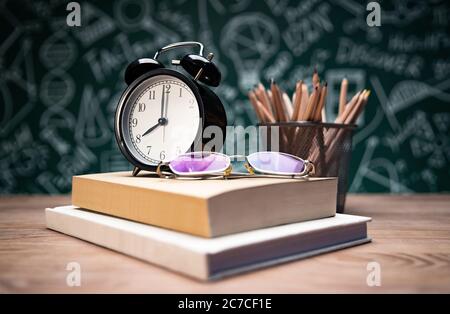 Vor der Tafel zeichnen Schulbedarf und Gläser auf dem Tisch Stockfoto