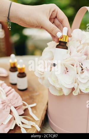 Geschäftsfrau Putting Flasche Serum in Box mit hellrosa Hortensien Blume, um Fotos für ihren Online-Shop zu machen Stockfoto