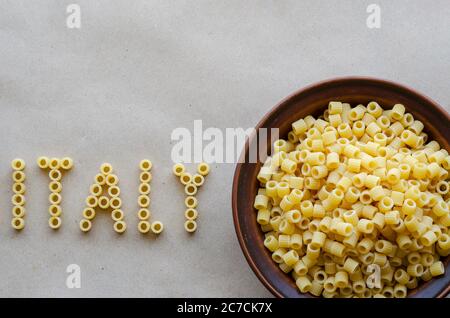 Wort Italien aus Großbuchstaben Englisch wird mit trockener Paste von Ditalini gelegt. Tonschüssel mit Pasta in der Nähe. Sorten von mediterranen Speisen. Blick von der Stockfoto