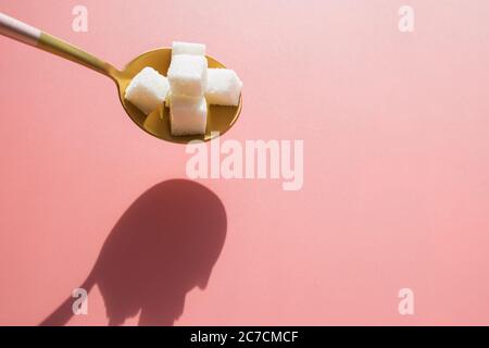 Zuckerwürfel in goldenem Metalllöffel auf rosa Hintergrund. Stockfoto