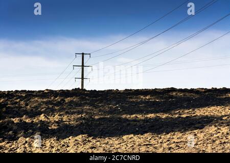 Stromleitungen erheben sich über einem gepflügten Feld unter einem klaren blauen Himmel bei Tageslicht, Auvergne Rhone Alpes, Frankreich Stockfoto