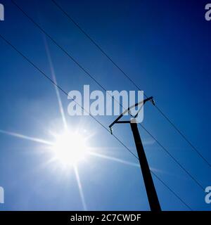 Helles Sonnenlicht, das über einem Strommast gegen einen klaren blauen Himmel während des Mittags in Frankreich leuchtet Stockfoto