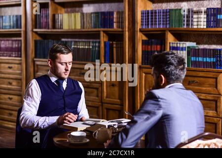 Herren im Anzug mit antiken Bücherregalen auf dem Hintergrund. Intelligente Männer, Wissenschaftler treffen sich in der Bibliothek. Professoren sprechen oder diskutieren Bildung in Vintage-Interieur. Intelligentes Elite- und Bildungskonzept. Stockfoto