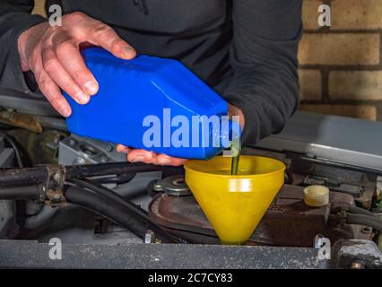 Nahaufnahme eines Mannes, der sich über den Flügel eines alten Autos in den Motorraum lehnt und Öl aus einem Plastikbehälter durch einen Trichter in den Motor gießt. Stockfoto