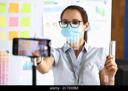 Maskierte Geschäftsfrau in einem Büro zeichnet Präsentation auf Smartphone Stockfoto