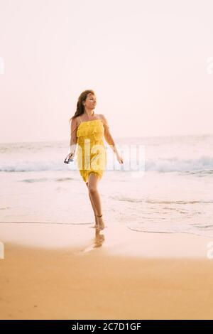 Goa, Indien. Junge Kaukasische Frau In Gelbem Kleid Wandern Auf Meeresküste Und Genießen Das Leben Im Sommer Sonnenlicht Stockfoto