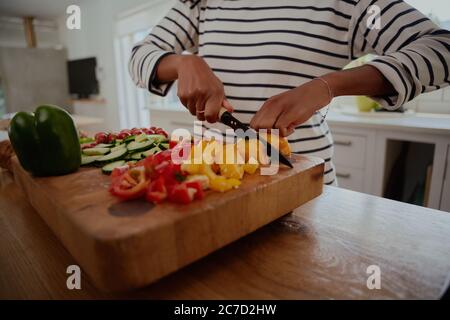 Nahaufnahme von Frau Hände hacken gelb und rot Paprika auf Holz Schneidebrett in der modernen Küche Stockfoto