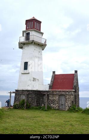 Weißer Leuchtturm mit einem roten Dach umgeben von viel Grün mit Ein Meer und Fischer im Hintergrund Stockfoto
