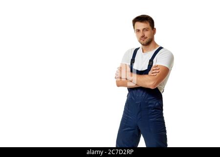 Junge kaukasische Arbeiter-Werkstatt in blauen Overalls mit Armen gefaltet isoliert auf weißem Studio-Hintergrund Stockfoto