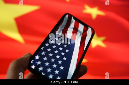 Chinesisch-amerikanische Wirtschaftsbeziehungen Konzept: Blick auf Hand halten Handy mit USA Flagge. Verschwommene Flagge von China Hintergrund. (Selektiver Fokus auf Stockfoto