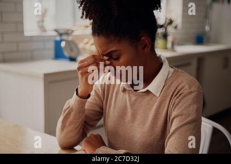 Frustrierte Frau sitzt auf dem Schreibtisch mit dem Hals und leidet unter Kopfschmerzen Stockfoto
