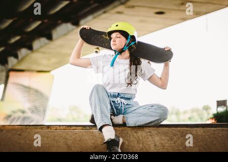 Schulmädchen nach Unterricht im Skateboarding Praxis im Outdoor-Skatepark. Stilvolle und schöne kaukasische Mädchen mit Skateboard auf einer Half-Pipe Rampe in Stockfoto