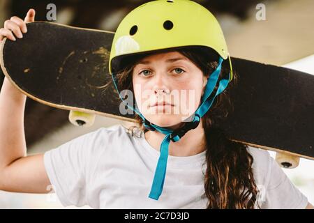 Schulmädchen nach Unterricht im Skateboarding Praxis im Outdoor-Skatepark. Stilvolle und schöne kaukasische Mädchen mit Skateboard auf einer Half-Pipe Rampe in Stockfoto