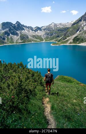Mann Silhouette bleiben auf scharfen Felsen Spitze. Wanderer zufrieden genießen Aussicht. Großer Mann auf felsigen Klippen, der auf einem blauen See, umgeben von Bergen, im Al beobachtet Stockfoto