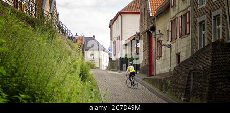 Weitaufnahme eines Kindes, das auf einem Fahrrad fährt Schmale Straße, umgeben von bunten Gebäuden Stockfoto