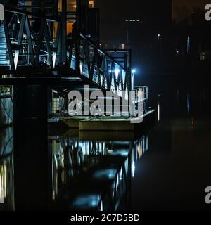 Vertikale Aufnahme von Metalltreppen mit Lichtern in der Nähe des Wassers Nachts Stockfoto