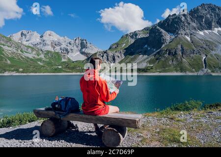 Rückansicht des Hipster Mann Fernweh Ruhe während des Wanderns sitzen mit Karte Blick auf Berge weit weg. Lifestyle Urlaubskonzept, Bergreisender Stockfoto