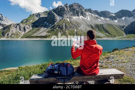 Rückansicht des Hipster Mann Fernweh Ruhe während des Wanderns sitzen mit Karte Blick auf Berge weit weg. Lifestyle Urlaubskonzept, Bergreisender Stockfoto