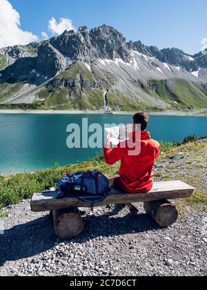 Rückansicht des Hipster Mann Fernweh Ruhe während des Wanderns sitzen mit Karte Blick auf Berge weit weg. Lifestyle Urlaubskonzept, Bergreisender Stockfoto