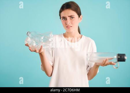 Verärgert Mädchen leider in Kamera halten Öko-und Plastikflaschen in den Händen über bunten Hintergrund isoliert suchen Stockfoto