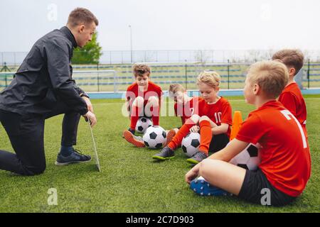 Gruppe von traurigen Jungen mit Trainer nach dem Verlust Fußballturnier Spiel. Kinder hören Junior-Level-Schule Fußballtrainer. Trainer erklärt Spieltakt Stockfoto