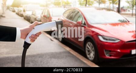 Hand mit Ladegerät auf einem Hintergrund von Elektroauto Stockfoto