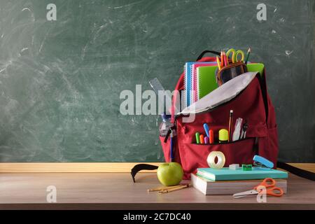 Rucksack voller Schulbedarf auf Holztisch und grüner Tafel mit Platz für Schreiben Vorderansicht Stockfoto